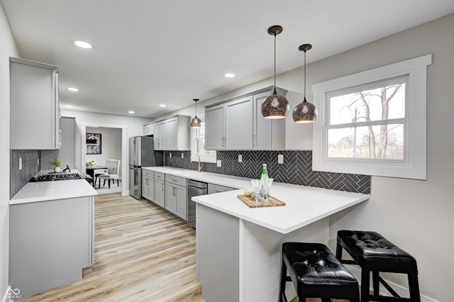 kitchen featuring pendant lighting, gray cabinetry, appliances with stainless steel finishes, kitchen peninsula, and a breakfast bar area