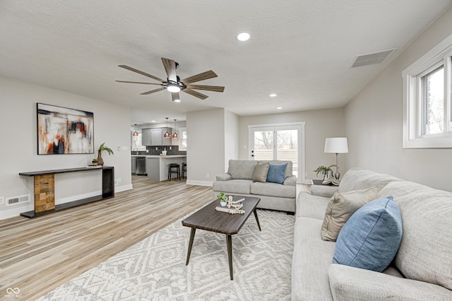 living room featuring ceiling fan, light hardwood / wood-style floors, and a textured ceiling