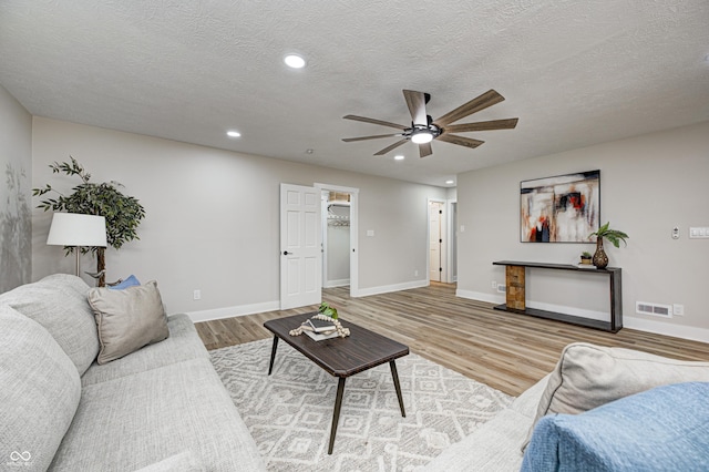 living room with ceiling fan, light wood-type flooring, and a textured ceiling