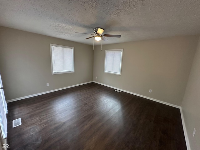 spare room with a textured ceiling, plenty of natural light, dark wood-type flooring, and ceiling fan