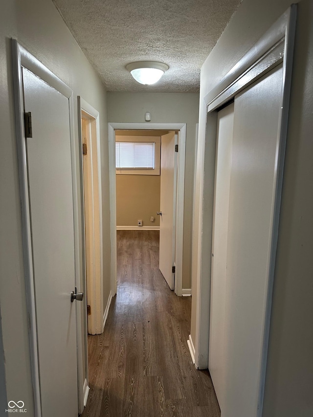 hallway with a textured ceiling and dark hardwood / wood-style floors