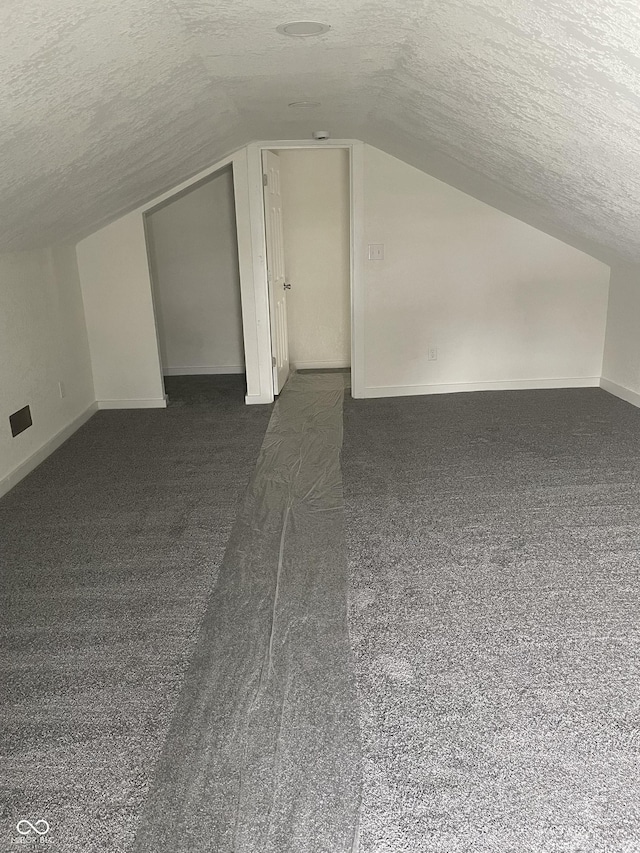 bonus room featuring dark colored carpet, a textured ceiling, and vaulted ceiling