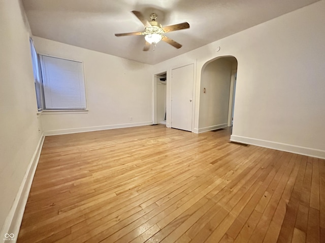 empty room featuring baseboards, arched walkways, light wood-style floors, and ceiling fan