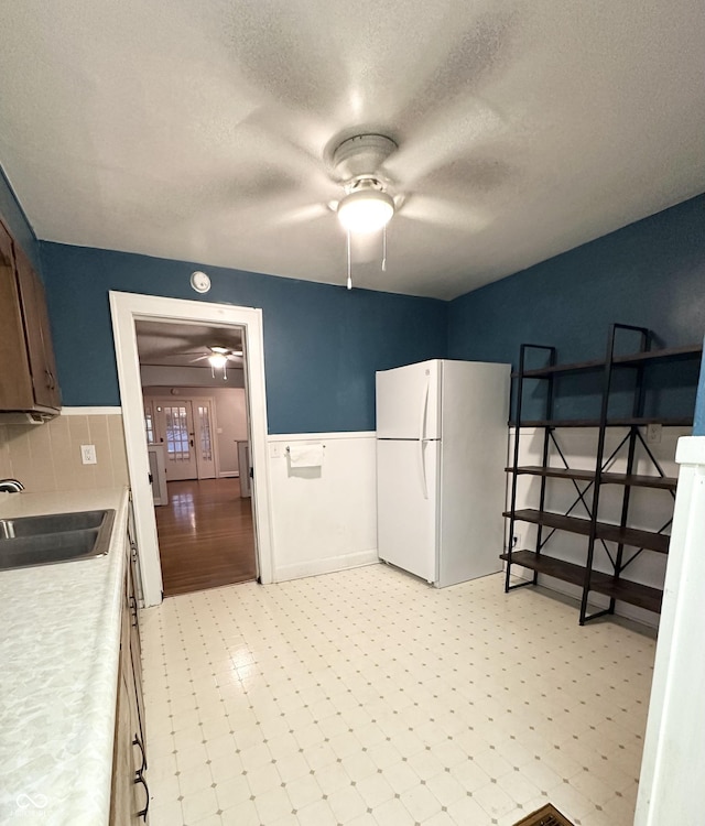 kitchen featuring a sink, light floors, a ceiling fan, and freestanding refrigerator