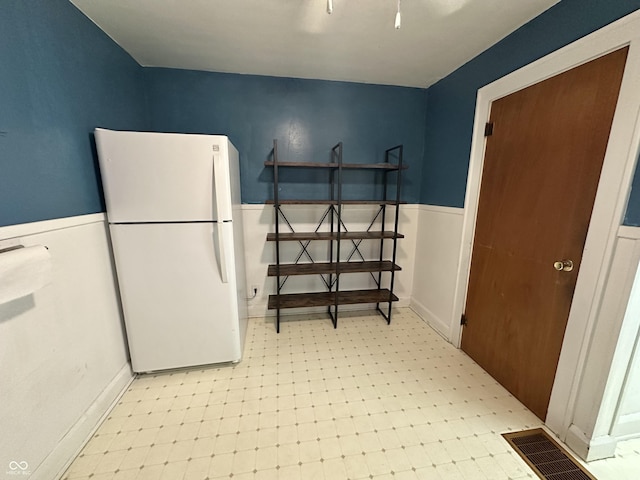interior space featuring a wainscoted wall, visible vents, light floors, and freestanding refrigerator