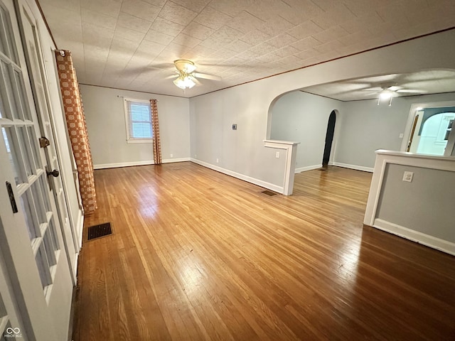 unfurnished room with hardwood / wood-style floors, a ceiling fan, arched walkways, and visible vents