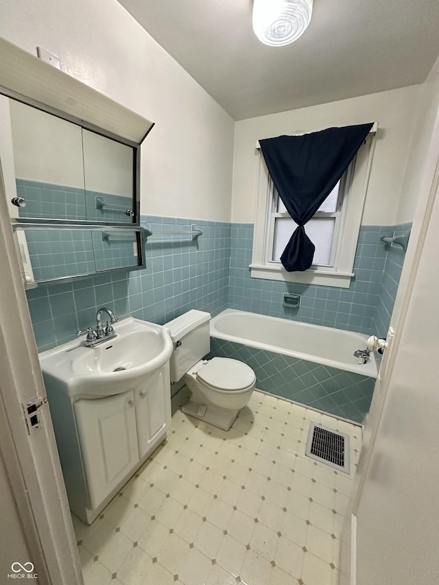 bathroom featuring toilet, vanity, tiled bath, visible vents, and tile walls
