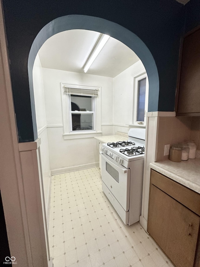 kitchen with arched walkways, white gas stove, light countertops, and light floors