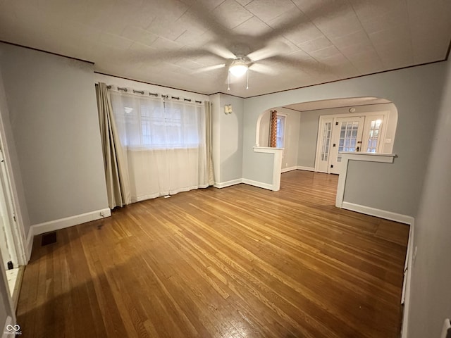 unfurnished room with wood-type flooring, arched walkways, baseboards, and visible vents