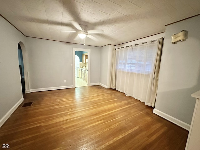 unfurnished room with arched walkways, visible vents, a ceiling fan, and wood finished floors