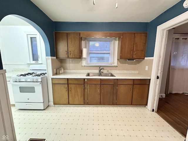 kitchen with white range with gas stovetop, light countertops, a sink, and light floors