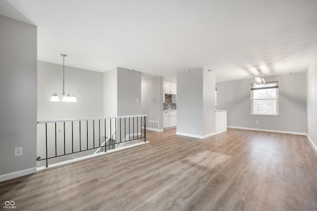 empty room featuring a notable chandelier and light wood-type flooring