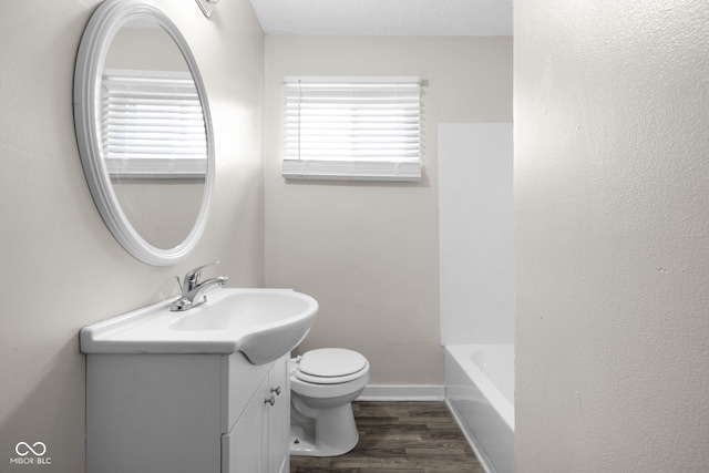 bathroom with a tub to relax in, vanity, toilet, and wood-type flooring