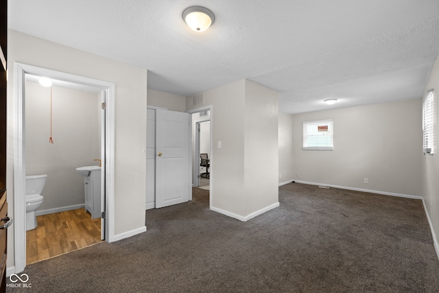 unfurnished bedroom with dark carpet, a textured ceiling, and ensuite bathroom