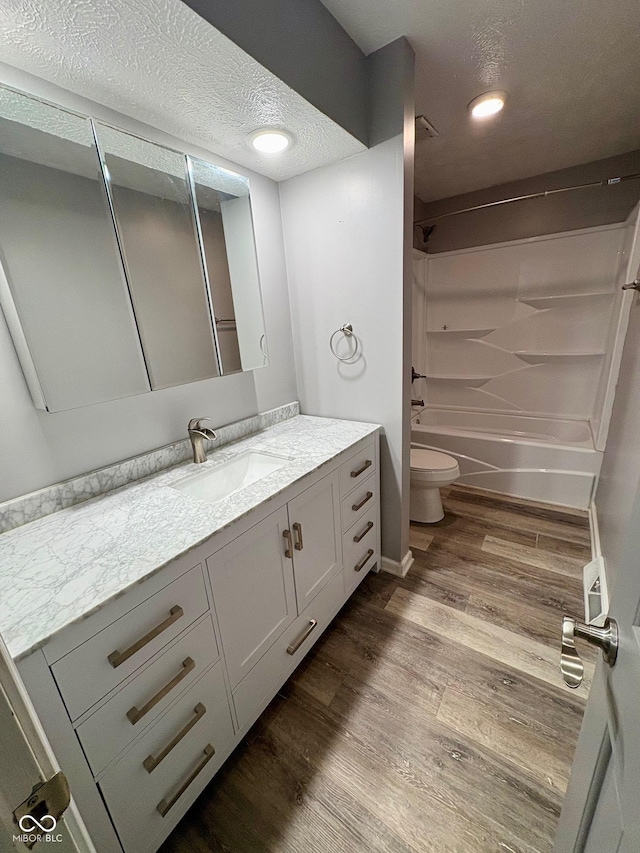 full bathroom with vanity, shower / washtub combination, toilet, a textured ceiling, and wood-type flooring