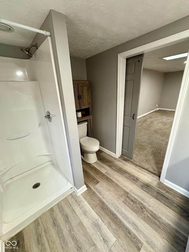 bathroom with hardwood / wood-style floors, toilet, a shower, and a textured ceiling