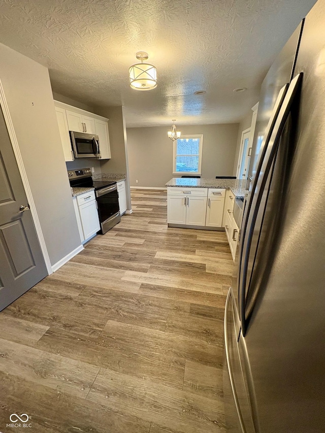 kitchen with light stone countertops, appliances with stainless steel finishes, light hardwood / wood-style flooring, a chandelier, and white cabinetry