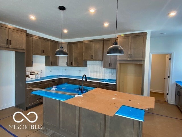 kitchen with an island with sink, decorative backsplash, light countertops, and hanging light fixtures