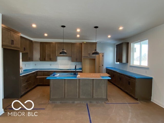 kitchen featuring pendant lighting, recessed lighting, light countertops, backsplash, and an island with sink