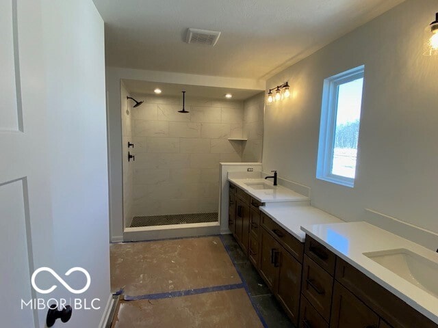 bathroom with double vanity, visible vents, a sink, and tiled shower