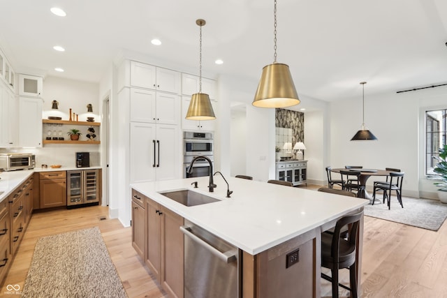 kitchen with decorative light fixtures, sink, white cabinets, a large island with sink, and stainless steel appliances