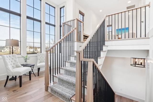 staircase with a high ceiling, a healthy amount of sunlight, hardwood / wood-style floors, and a chandelier