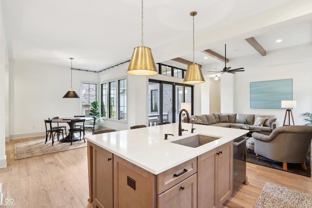 kitchen with a kitchen island with sink, sink, decorative light fixtures, and light wood-type flooring