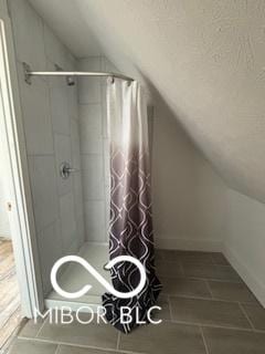 bathroom with tile patterned flooring, walk in shower, and lofted ceiling