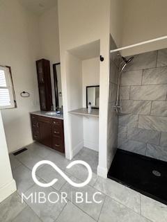 bathroom with a tile shower, vanity, and tile patterned floors