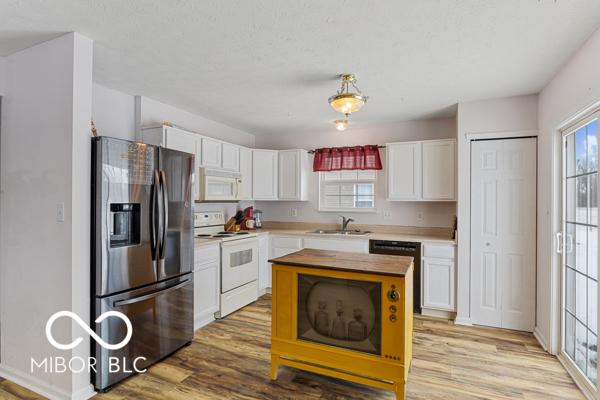 kitchen with white appliances, a kitchen island, sink, light hardwood / wood-style flooring, and white cabinetry