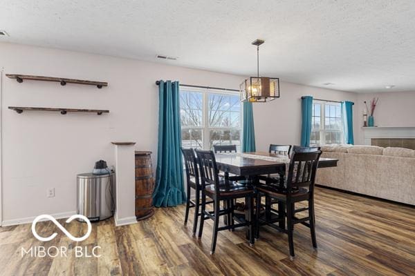 dining room with a textured ceiling, dark hardwood / wood-style flooring, an inviting chandelier, and a tiled fireplace