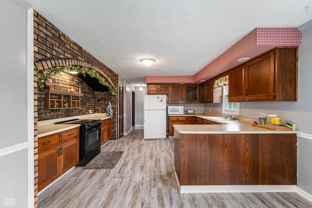 kitchen with white appliances, kitchen peninsula, brick wall, and light hardwood / wood-style flooring