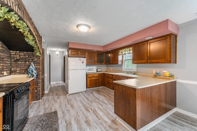 kitchen featuring white appliances, sink, light hardwood / wood-style flooring, a textured ceiling, and kitchen peninsula