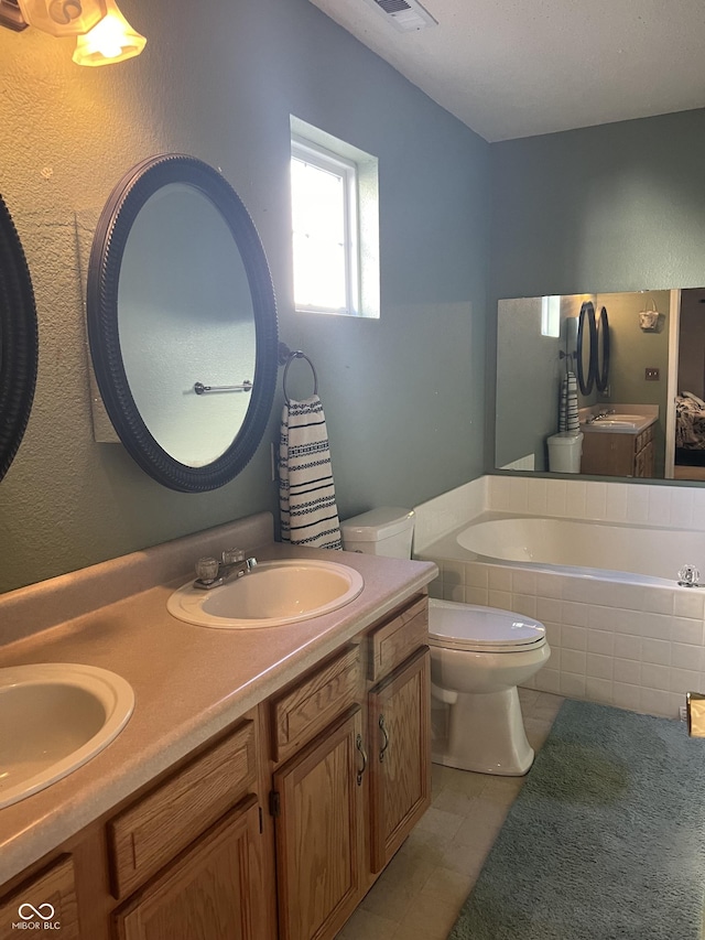 bathroom with tiled tub, vanity, tile patterned floors, and toilet