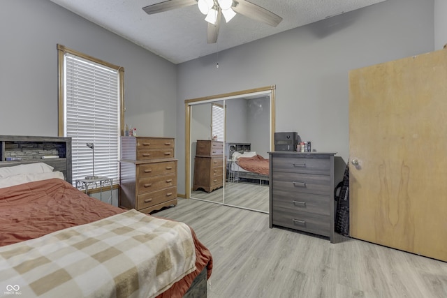 bedroom with a textured ceiling, light hardwood / wood-style floors, a closet, and ceiling fan