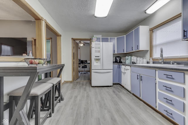 kitchen with a textured ceiling, white appliances, blue cabinets, sink, and light hardwood / wood-style flooring