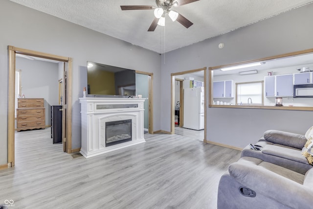 living room featuring ceiling fan, light hardwood / wood-style floors, sink, and a textured ceiling