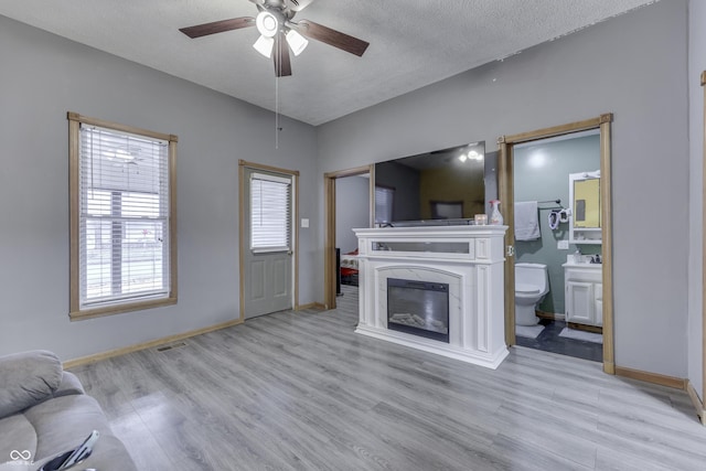 living room featuring ceiling fan, light wood-type flooring, and a textured ceiling