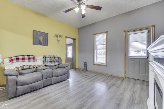 living room featuring ceiling fan, light hardwood / wood-style floors, and a textured ceiling