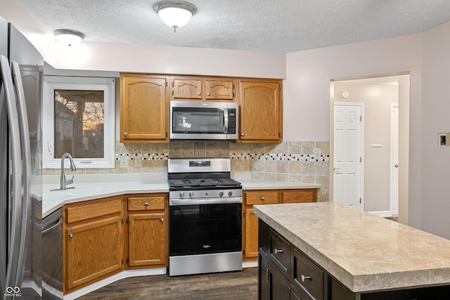 kitchen with appliances with stainless steel finishes, tasteful backsplash, a textured ceiling, dark wood-type flooring, and sink