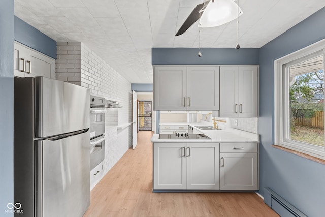 kitchen with a baseboard heating unit, sink, light wood-type flooring, stainless steel appliances, and brick wall