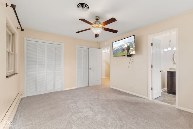 unfurnished bedroom with connected bathroom, ceiling fan with notable chandelier, a baseboard heating unit, light colored carpet, and two closets