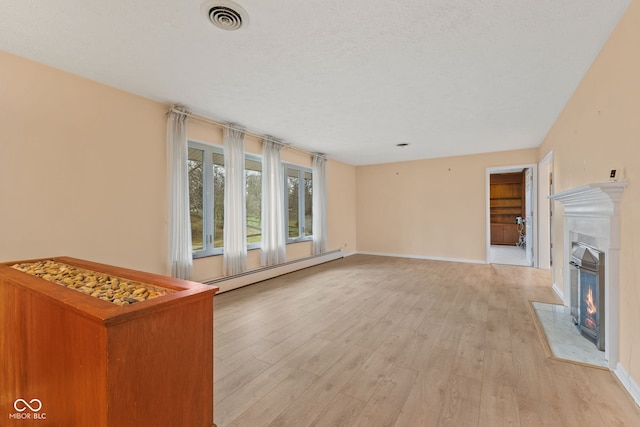 unfurnished living room with a textured ceiling, light hardwood / wood-style flooring, and a baseboard heating unit