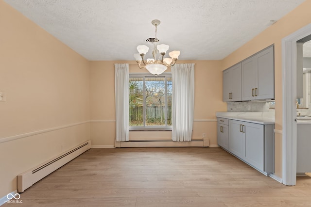 unfurnished dining area with a chandelier, light hardwood / wood-style flooring, and a baseboard heating unit