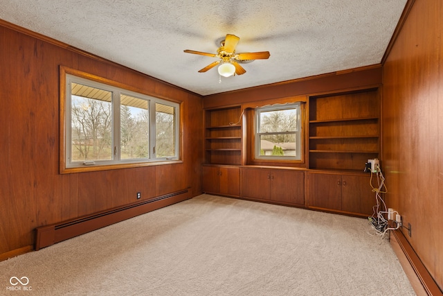 unfurnished room featuring light carpet, a baseboard radiator, a healthy amount of sunlight, and wood walls