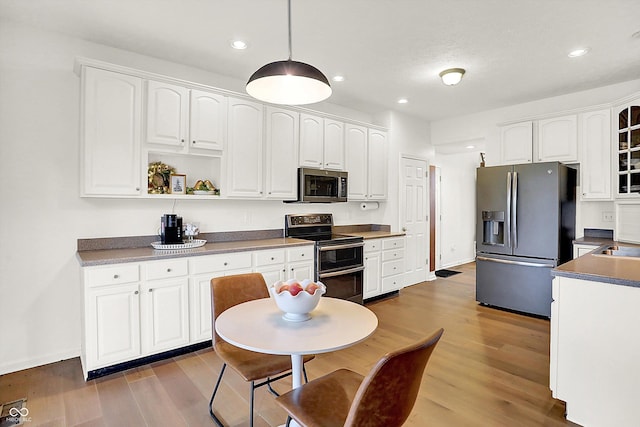 kitchen featuring white cabinetry, wood-type flooring, decorative light fixtures, and appliances with stainless steel finishes