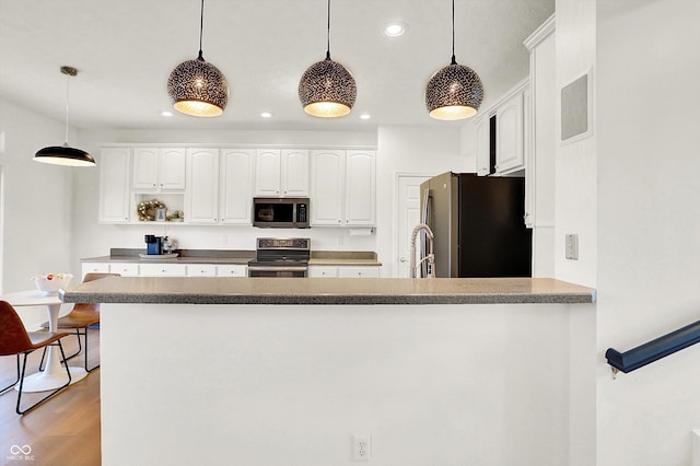 kitchen featuring white cabinets, kitchen peninsula, hanging light fixtures, appliances with stainless steel finishes, and wood-type flooring