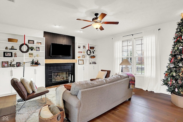 living room featuring ceiling fan, a large fireplace, and dark hardwood / wood-style floors