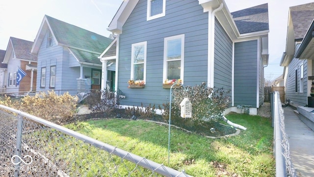 view of side of property with a shingled roof, a yard, and fence