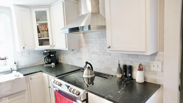 kitchen featuring stainless steel electric range, glass insert cabinets, white cabinetry, wall chimney range hood, and tasteful backsplash